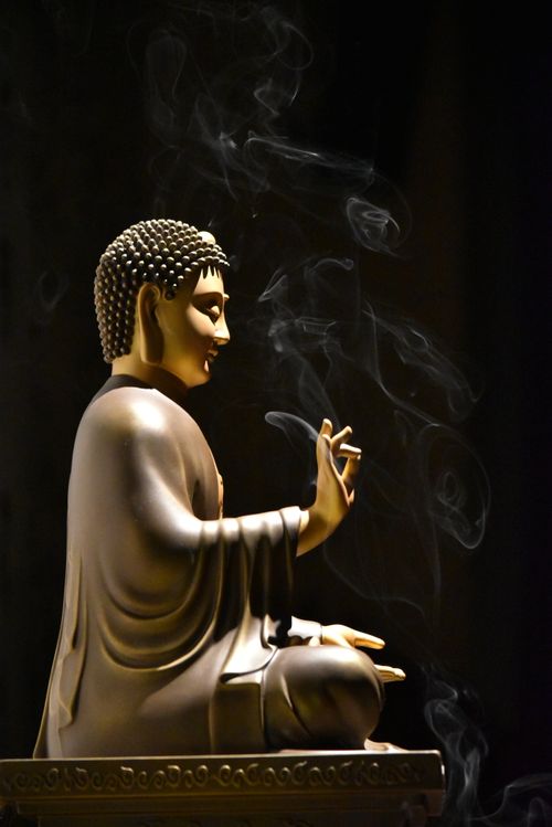 Free Side profile of a Buddha statue with incense smoke rising against a dark background. Stock Photo