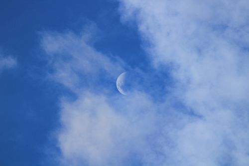 Free A serene view of the crescent moon surrounded by fluffy clouds in a bright blue sky. Stock Photo