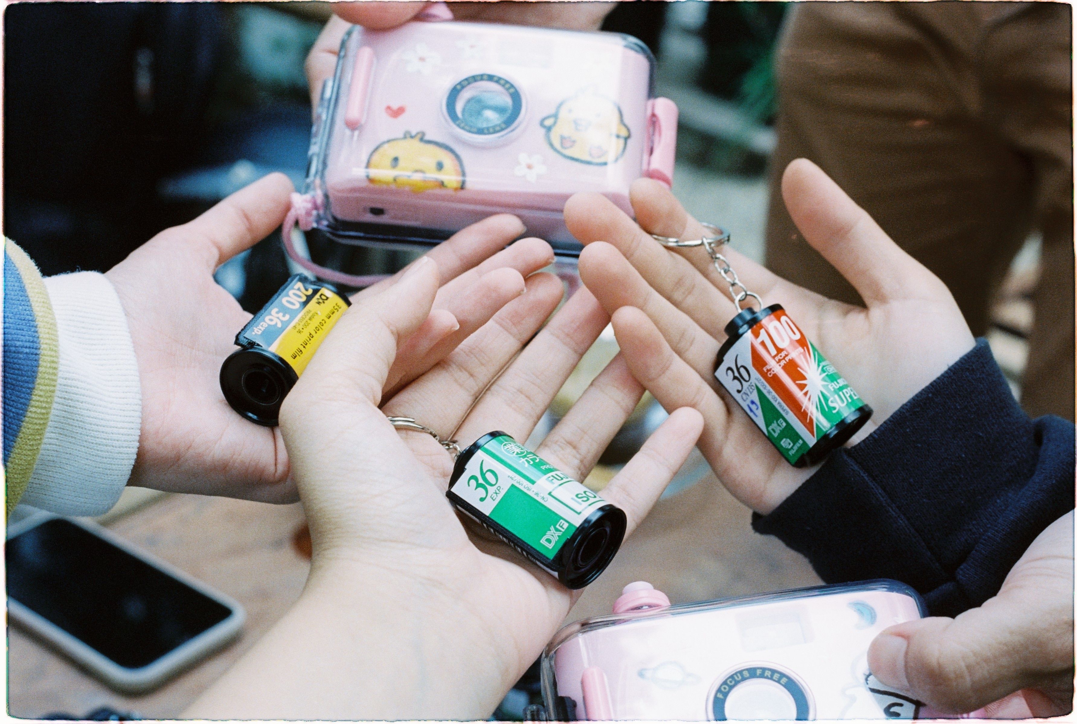 A close-up of hands holding various film roll keychains with a playful camera case.