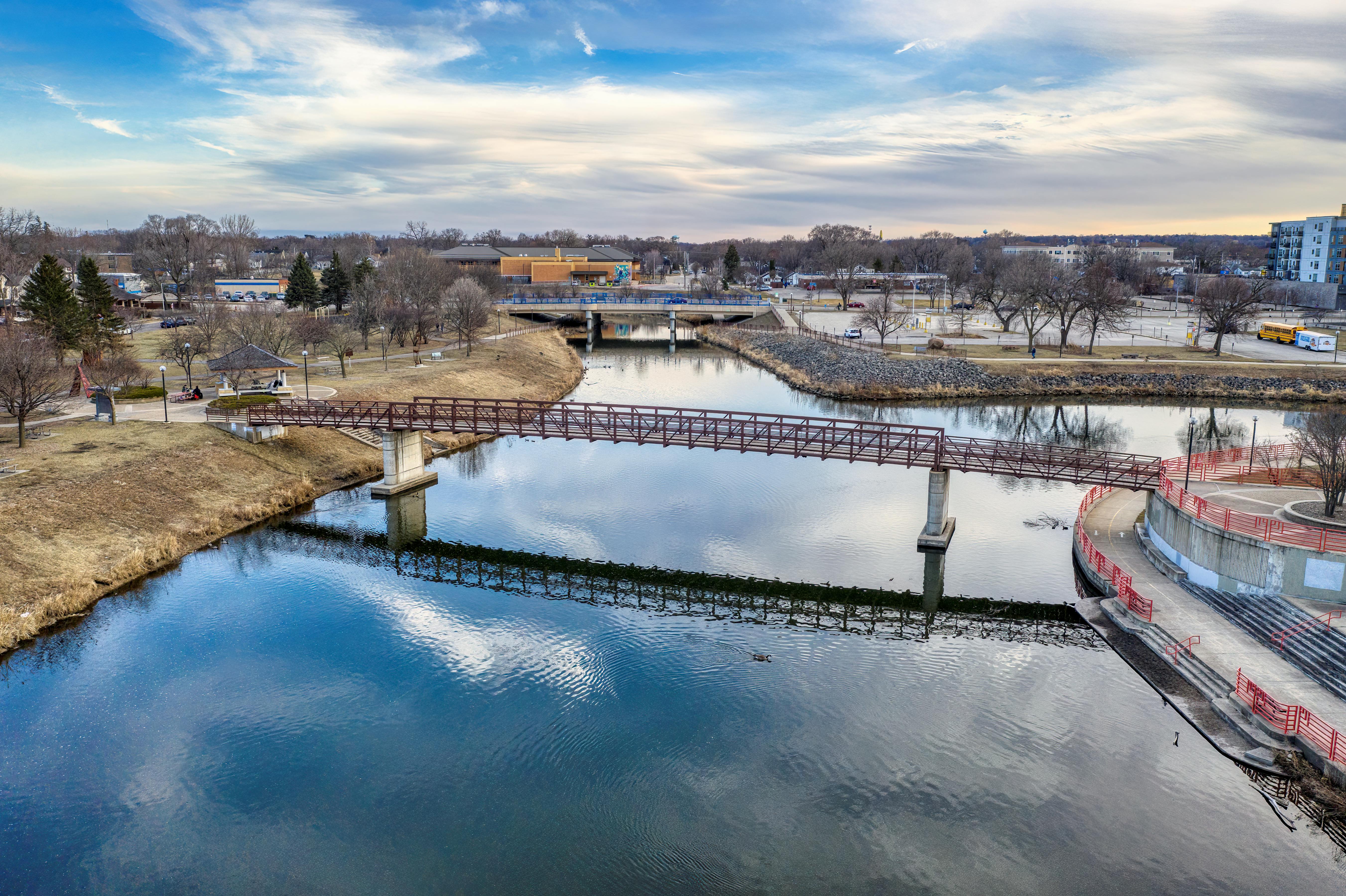 A tranquil view of a pedestrian bridge over a river reflecting the cloudy sky in Rochester, MN.
