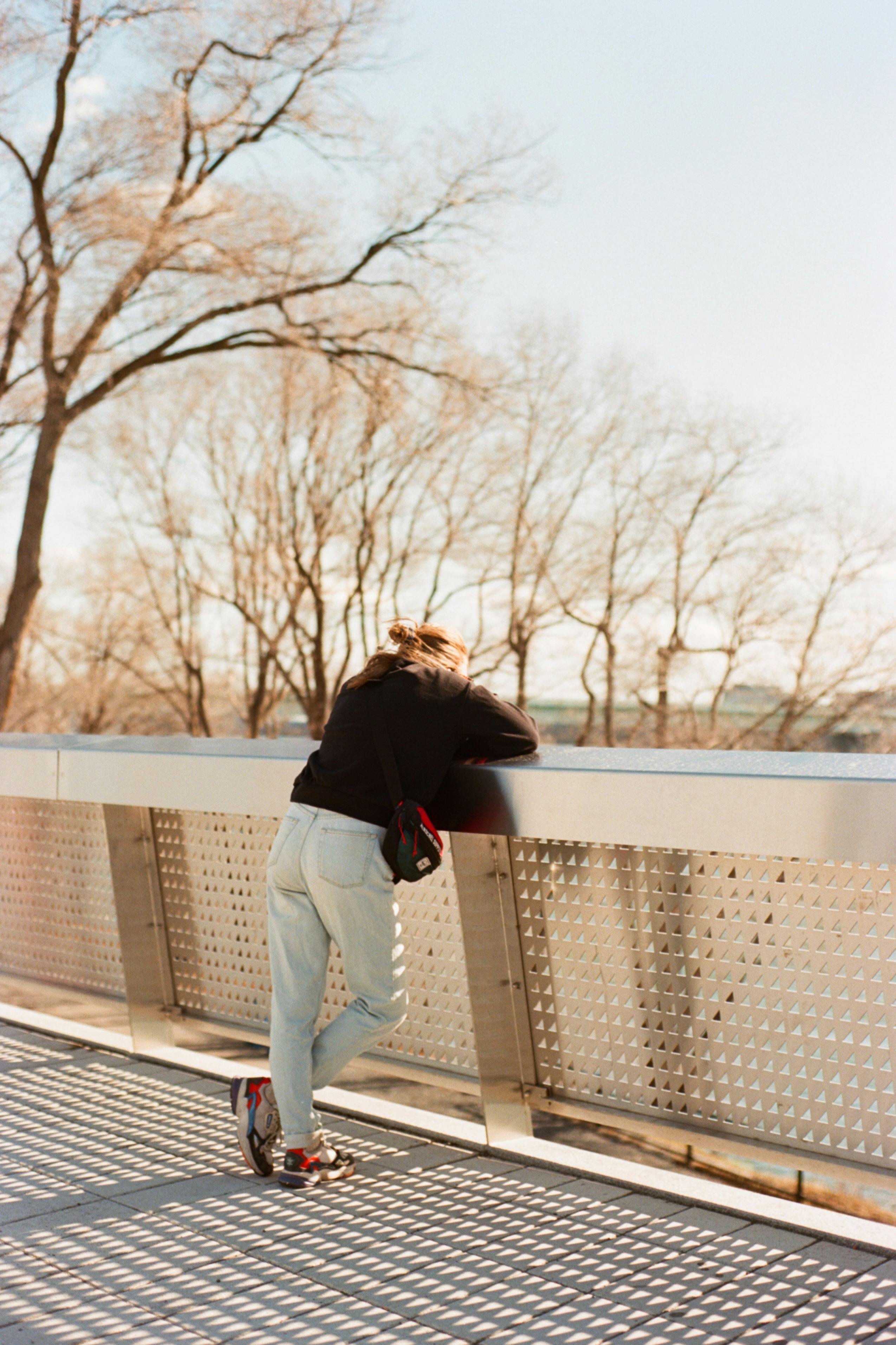 a woman in a black sweater and denim pants leaning on a railing