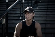 一个戴着纽约棒球帽的健康年轻人坐在城市台阶上，散发着现代又酷的氛围