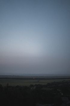 A tranquil rural landscape at dusk featuring fog over fields and a soft evening sky.