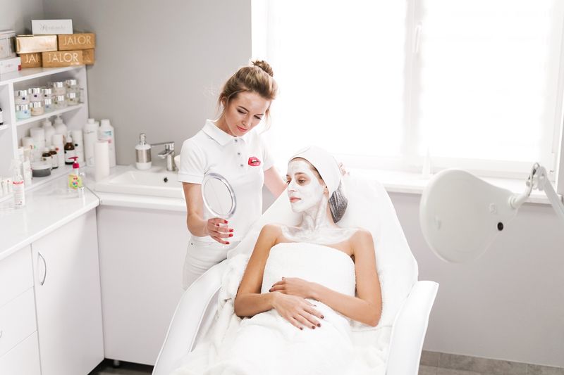 Beautician applying a facial mask to a client in a modern salon. Professional skincare service indoors.