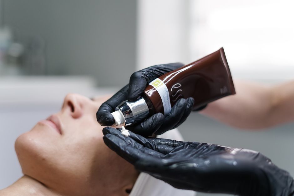 Handskbeklädd hand håller en hudvårdskräm – rätt eftervårdsprodukter är avgörande efter microneedling