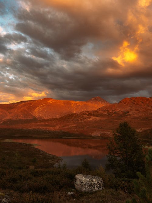 Brown Mountains Near Lake Under Dark Cloudy Sky