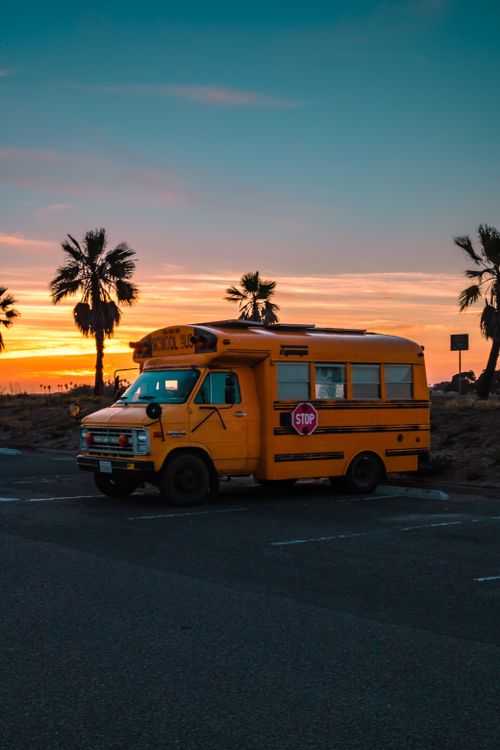 Free A parked vintage school bus amidst palm trees during a vibrant sunset, creating a nostalgic tropical vibe. Stock Photo