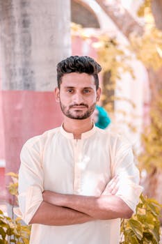 一位自信的南亚男子留着胡须，身着传统服装，在自然环境中摆出姿势，展现现代时尚