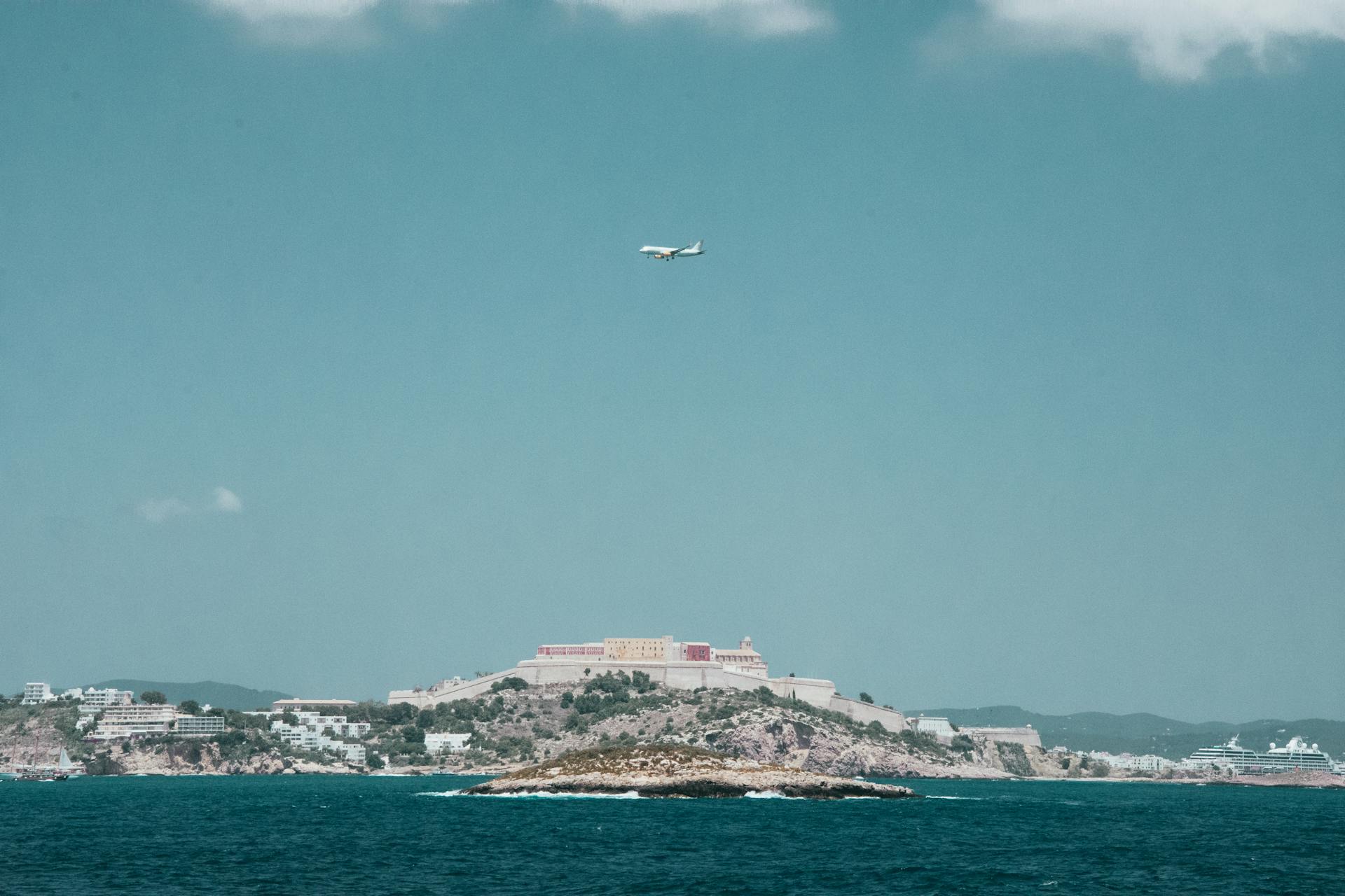 White Airplane Flying over a City Under Blue and White Cloudy Sky