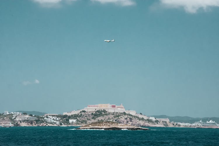 White Airplane Flying Over A City Under Blue And White Cloudy Sky