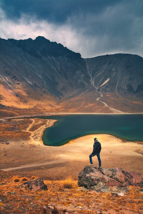 Free Man stands on rock, gazing at beautiful mountain lake in Mexico's rugged landscape. Stock Photo