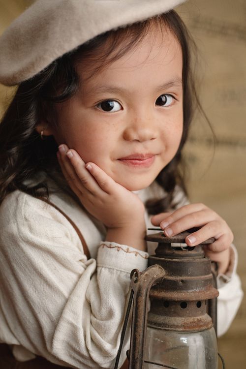 Free Charming young girl with a beret and lantern, exuding warmth and curiosity. Stock Photo