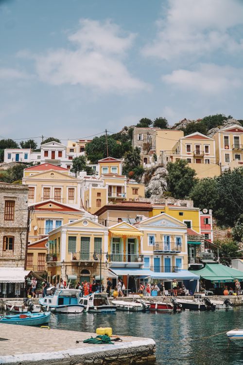 Free Vibrant houses on the Symi waterfront with boats and hills in the background, Greece. Stock Photo