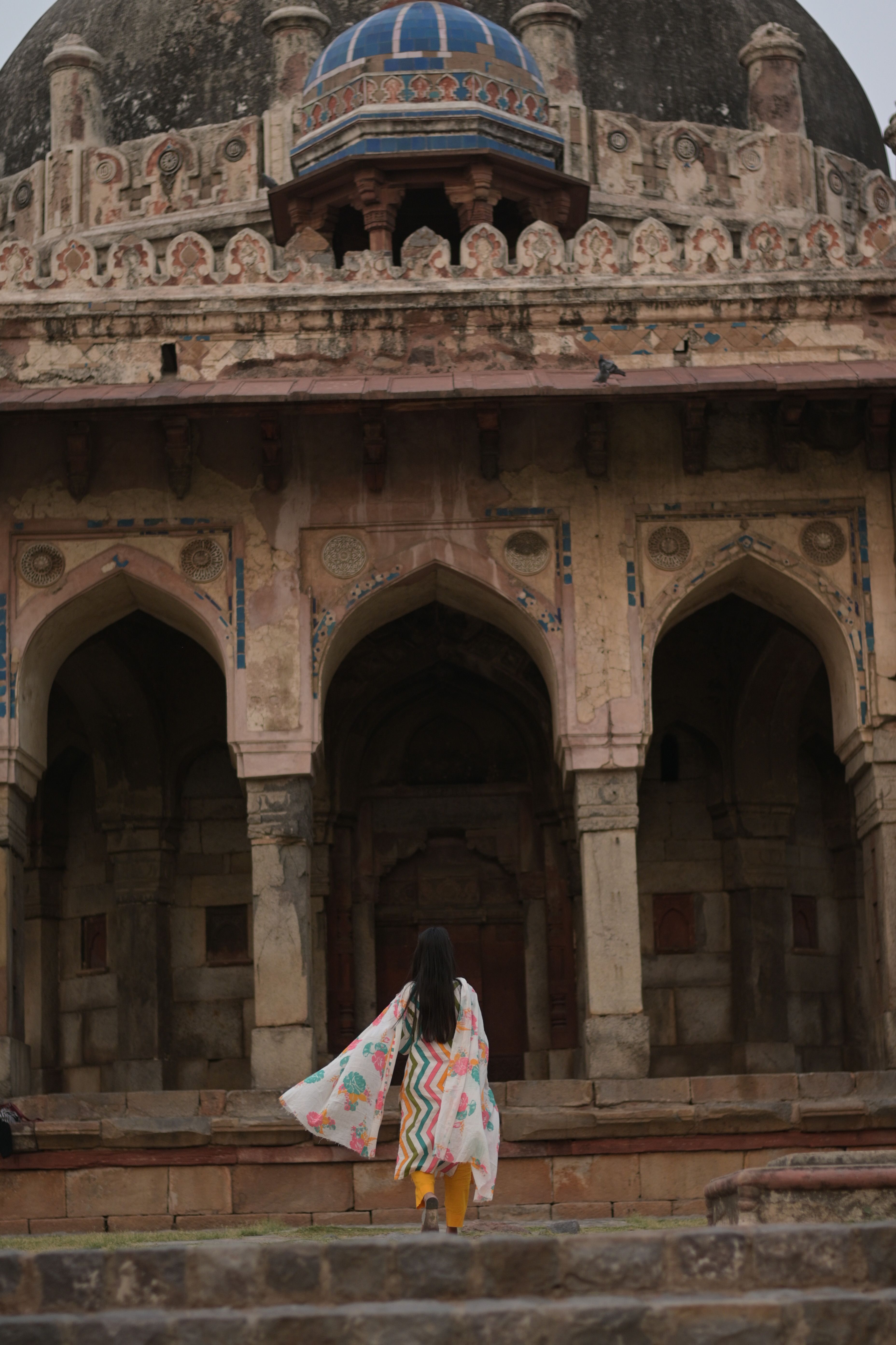 Back view of a woman standing before the ancient Tomb of Isa Khan in Delhi, India.