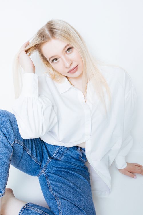 Free Portrait of a blonde woman in blue jeans and white shirt, hand through hair, on white background. Stock Photo