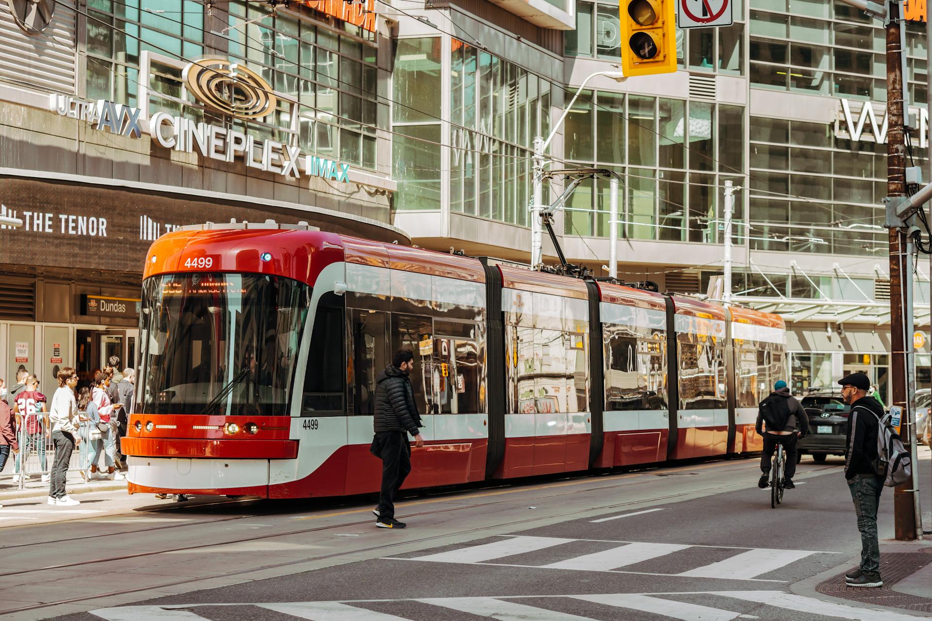 Red streetcar in Toronto at Dundas Square with pedestrians and cyclists in an urban setting.