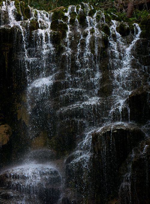 Free A peaceful waterfall cascading over lush, moss-covered rocks in nature's embrace. Stock Photo