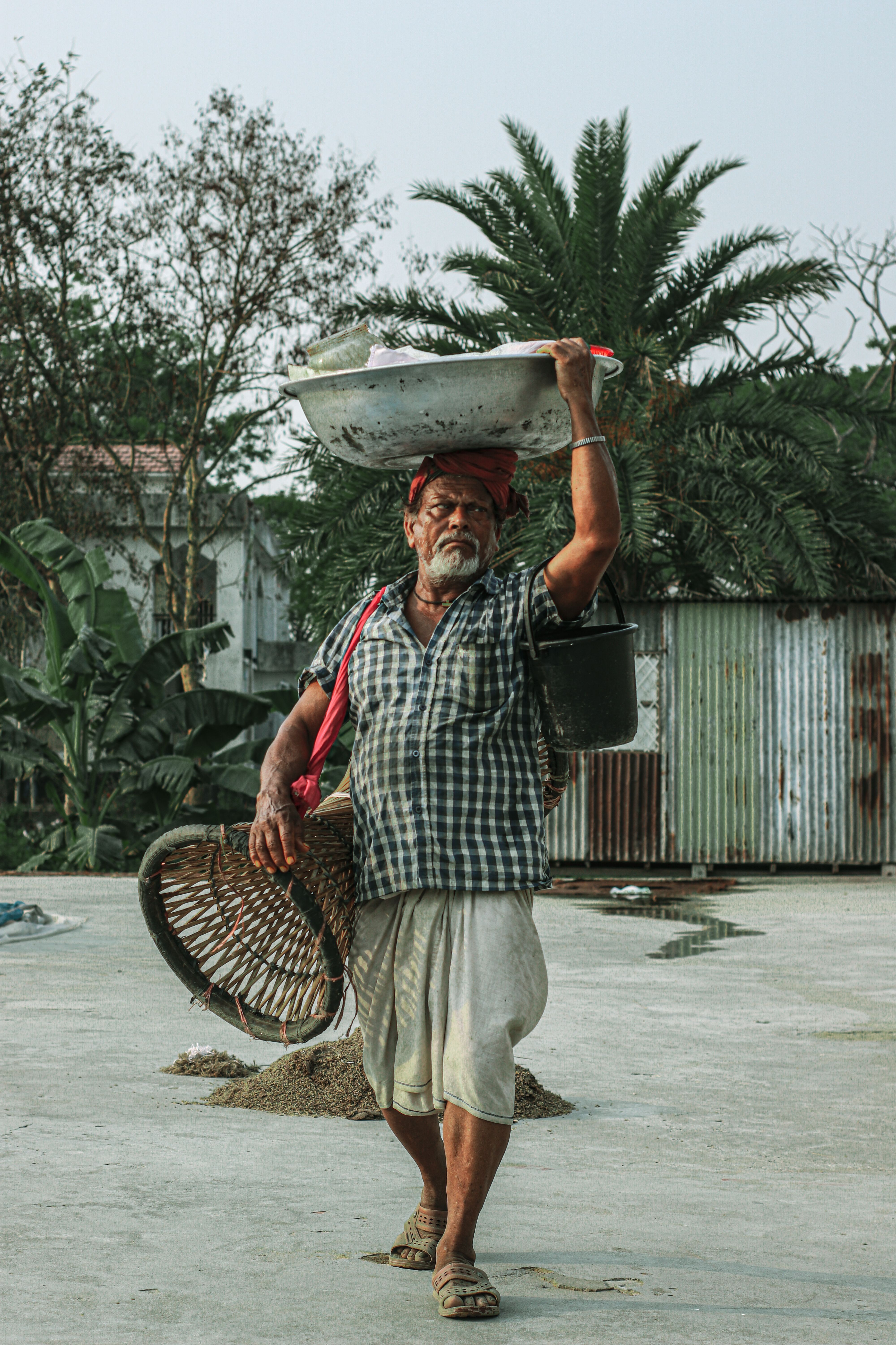 Elderly man carrying a basket and tools outdoors, showcasing traditional labor.