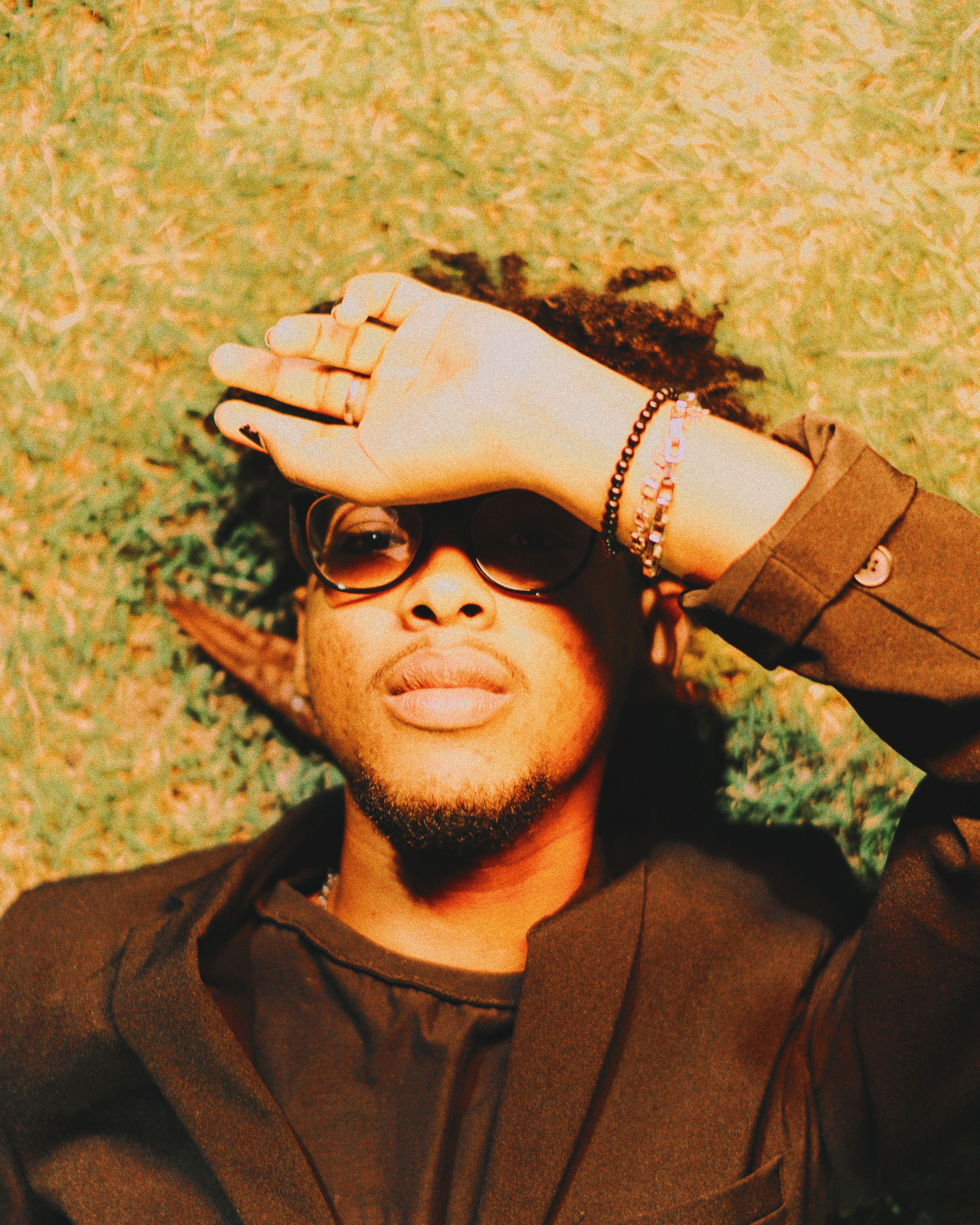 Portrait of a young man in sunglasses resting on grass with hand shielding his eyes from the sun.