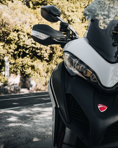 Free Front view of a modern motorcycle under trees, showcasing sleek headlights and design. Stock Photo