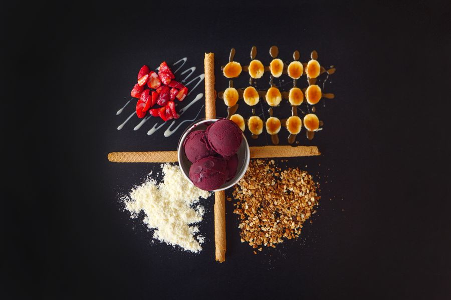 Flat lay of ice cream with strawberries, nuts, and wafers on a black background.