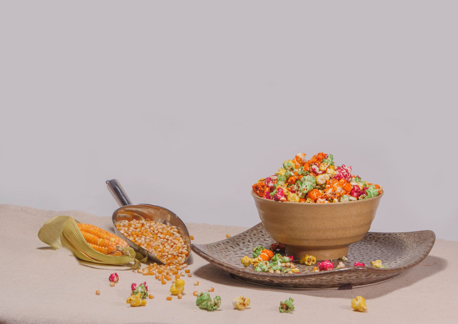 Vibrant rainbow popcorn in a bowl with corn kernels on a woven mat.