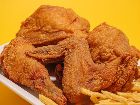 Delicious crispy fried chicken alongside golden French fries on a vibrant yellow backdrop.