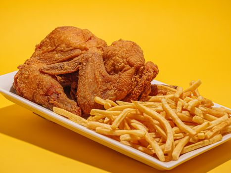 A classic platter of crispy fried chicken and golden French fries on a yellow background.
