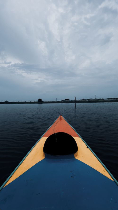 Free A vibrant kayak on a serene lake under a cloudy sky, perfect for outdoor adventure lovers. Stock Photo