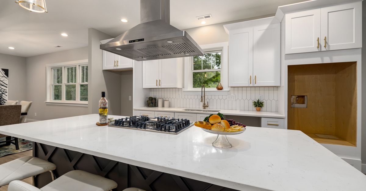 Modern kitchen with white cabinets, dark island, and stainless steel range hood.