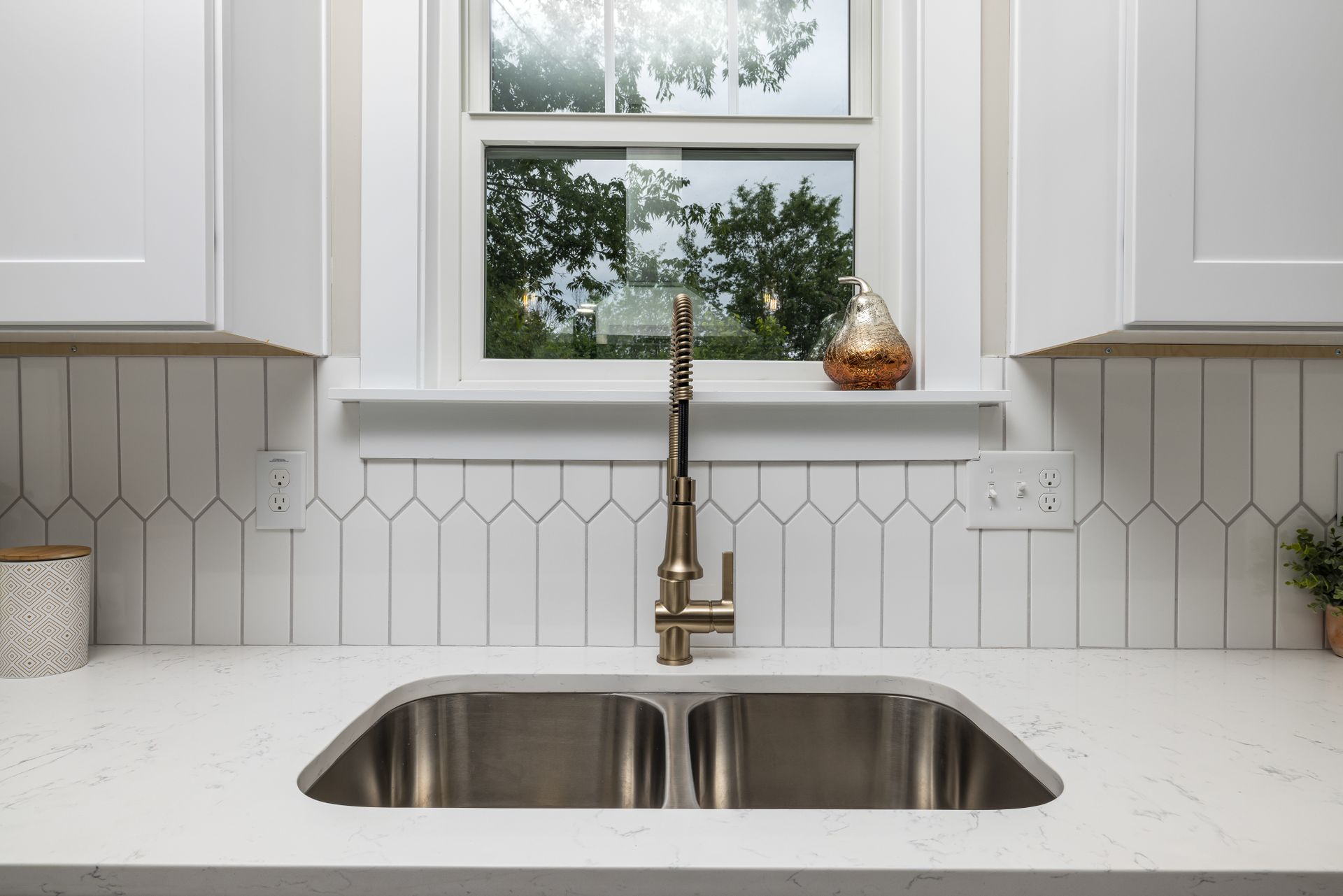 Contemporary kitchen design featuring white cabinets and a stainless steel sink with a minimalist faucet.
