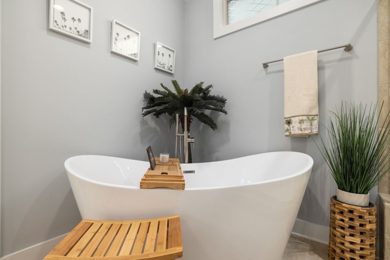 Pale blue cottage bathroom with a white freestanding bath, a wooden bath board, a bamboo stool and a woven basket