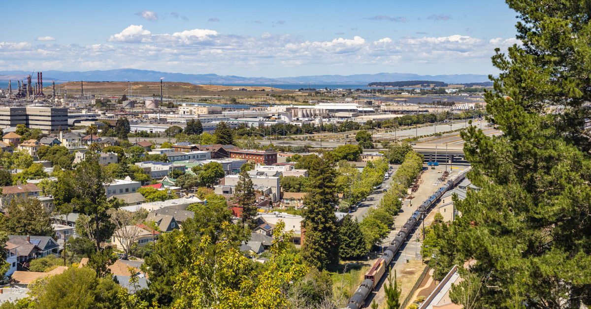 A scenic view of a town with industrial buildings in the distance under a clear blue sky.