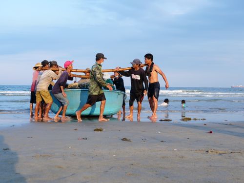 Free A group effort as men work together to pull a boat ashore on a sunny beach. Stock Photo