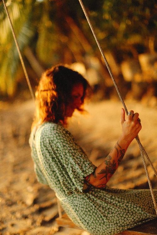 Free Tattooed woman in green dress swinging outdoors, basking in warm sunset light. Stock Photo