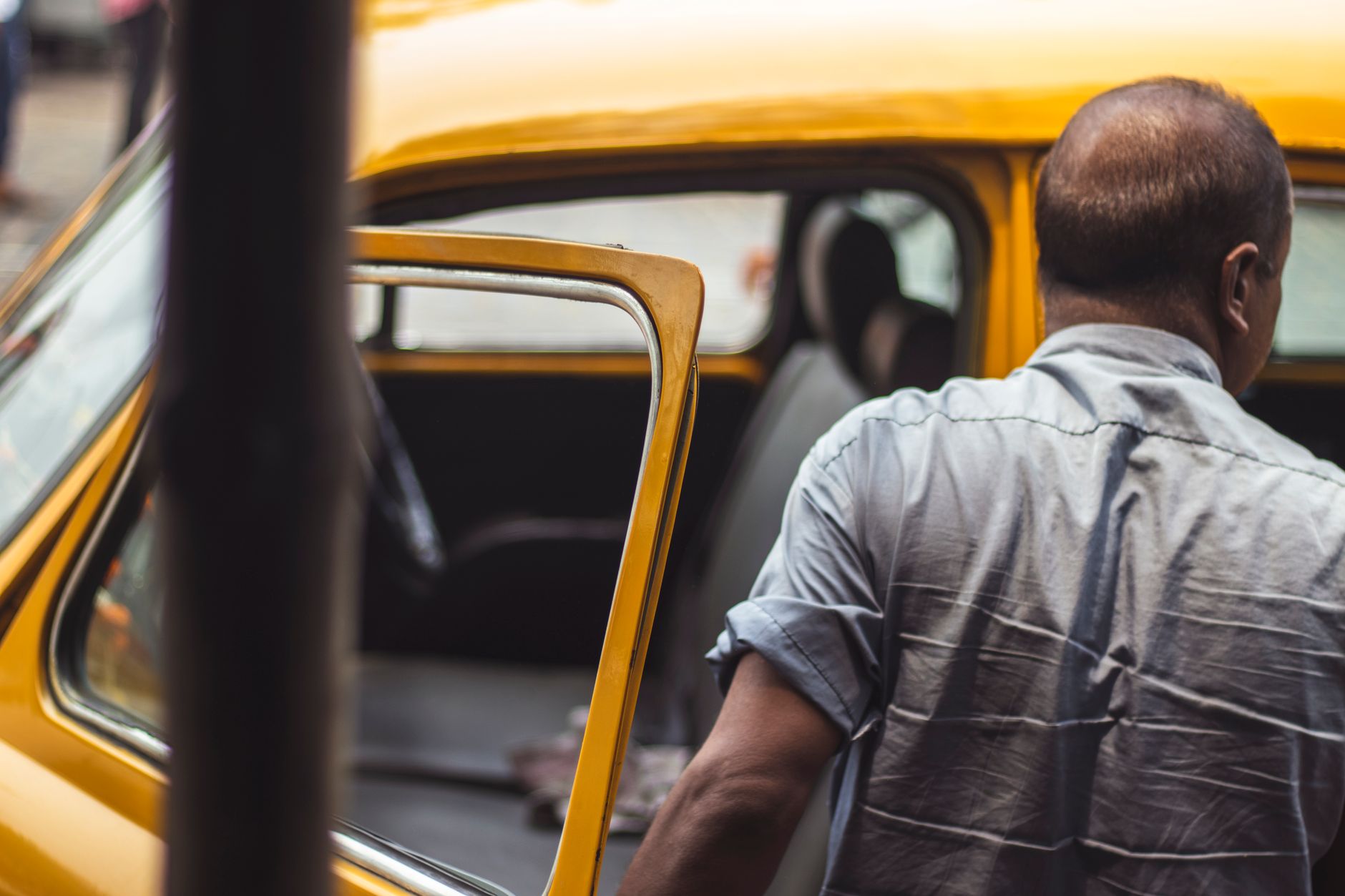 Back view of a man opening the door of a parked yellow car.