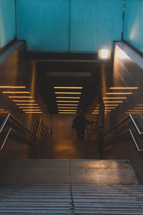 Free A lone commuter descends illuminated stairs in Bucharest's underground station, captured in a moody light. Stock Photo