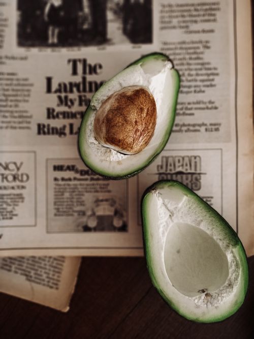 Free A fresh halved avocado displayed on a vintage newspaper, creating a rustic food photography scene. Stock Photo