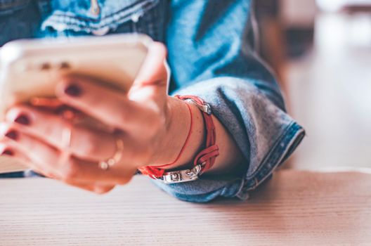 A person wearing a denim jacket and wristwatch uses a smartphone in a casual setting.