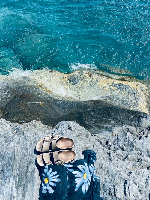 Free View of a Greek coastline with sandals and floral dress on rocks by the sea edge. Stock Photo
