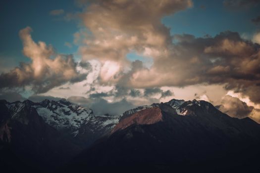 Stunning mountain peaks under a dramatic cloudy sky at twilight, perfect for scenic nature backgrounds.