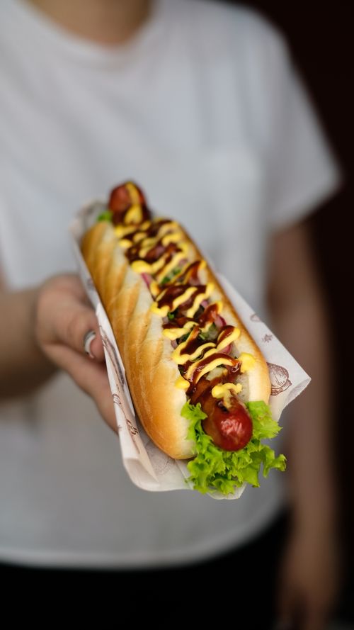 Free Delicious gourmet hot dog with mustard and ketchup held by a person wearing white. Stock Photo