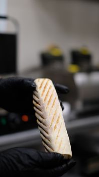 Close-up of a chef's hands holding a grilled wrap in a kitchen. Gloved hands emphasize hygiene.