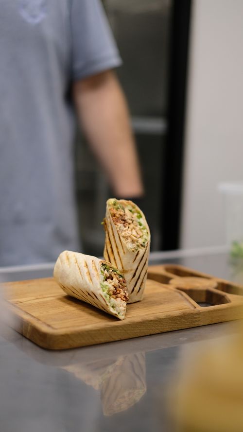 Free Appetizing grilled burrito on a cutting board in the kitchen with a blurred person in the background. Stock Photo