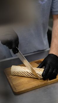 Chef cutting a grilled tortilla wrap on a wooden board in a professional kitchen setting.