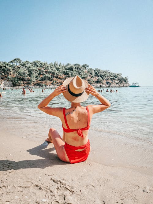Woman in Red Bikini Wearing a Straw Hat Sitting on Shore