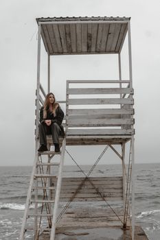 A solitary woman seated on a lifeguard tower overlooking a beach under a cloudy sky.