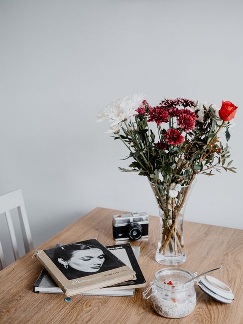 Minimalist still life featuring a vase of flowers, books, and a vintage camera on a wooden table.