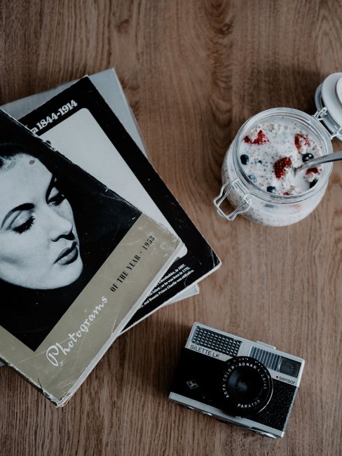 Flat lay of a vintage photography book and oatmeal in a jar on a wooden table.