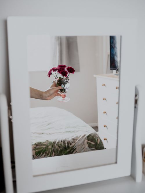 Free A delicate reflection of a hand holding vibrant flowers in a bedroom mirror. Stock Photo